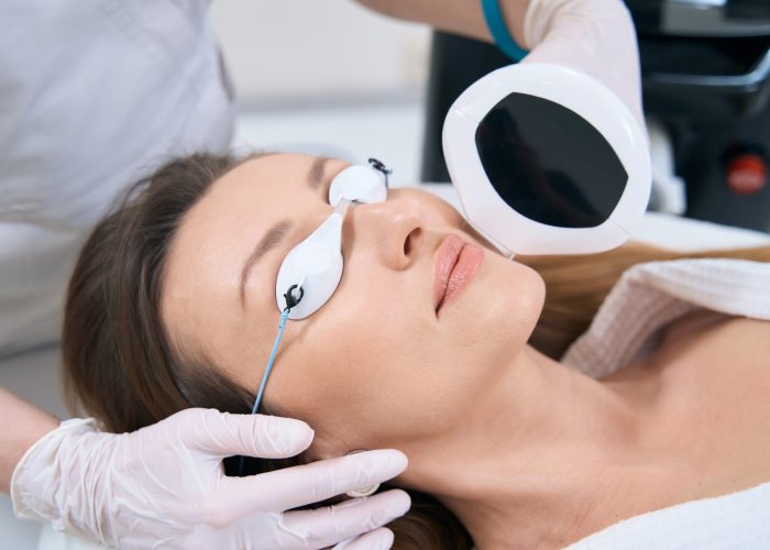 Adult woman in protective glassesduring skin rejuvenation procedure on phototherapy for facial skin rejuvenation